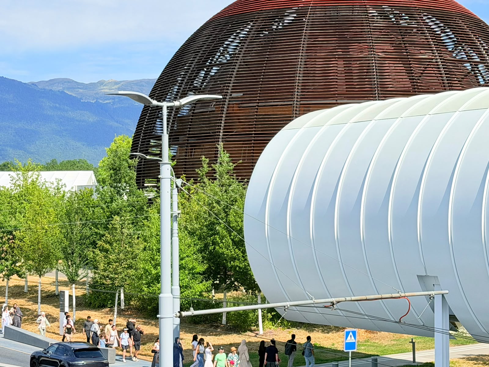 A ribbed cylindrical structure beside a dark slatted dome on a walkway