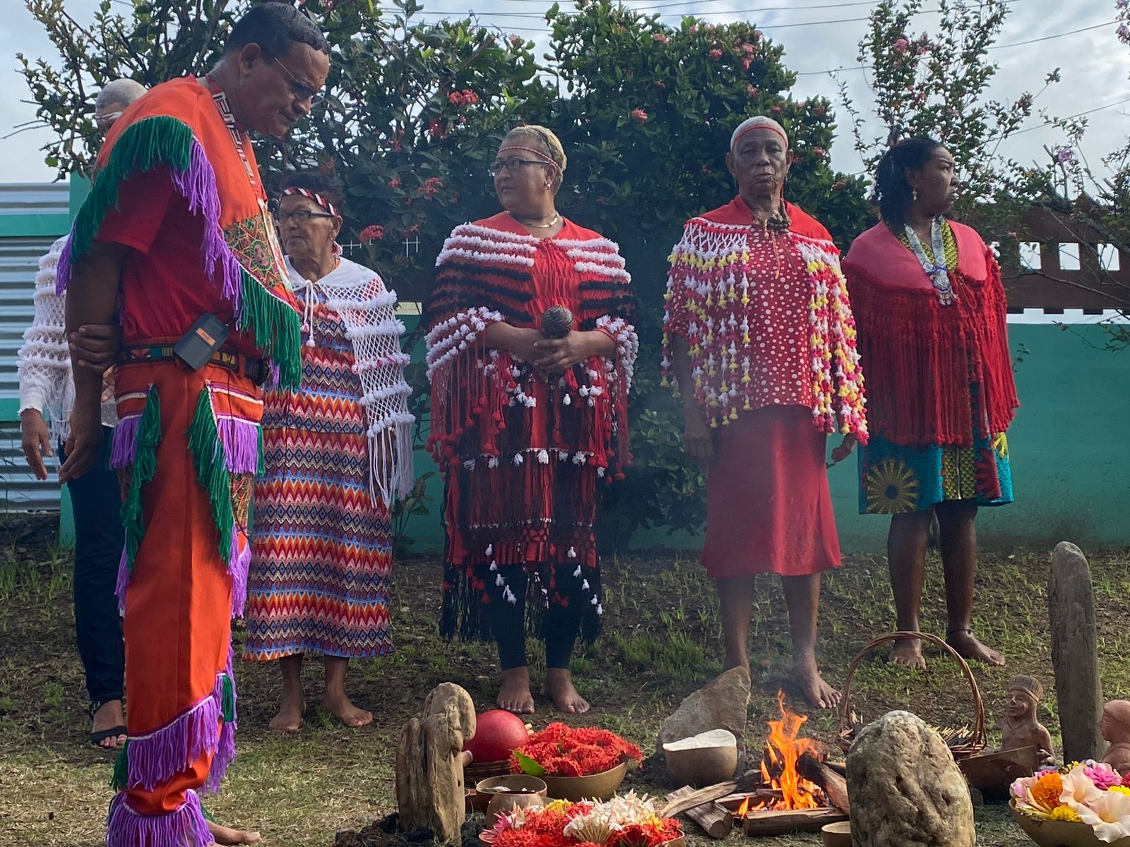 An indigenous ceremony around a fire, participants in woven red garments