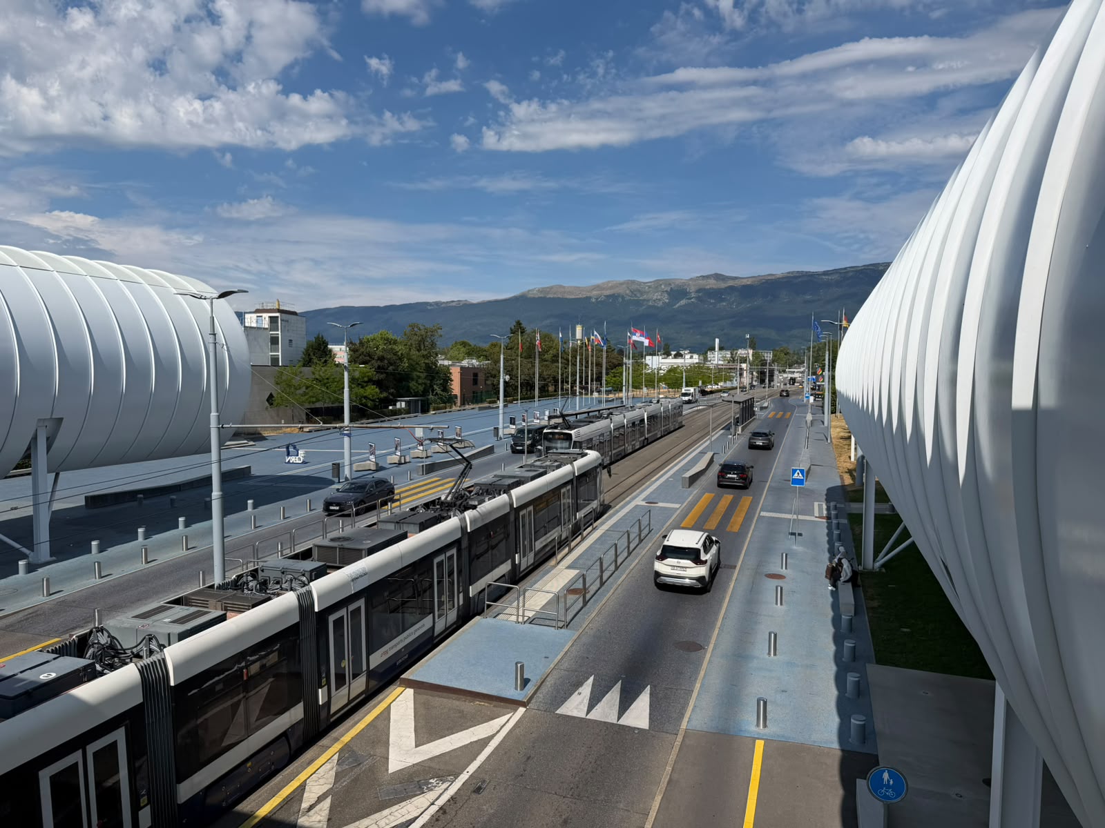 A modern tram passing through an urban transit hub framed by white ribbed tubes