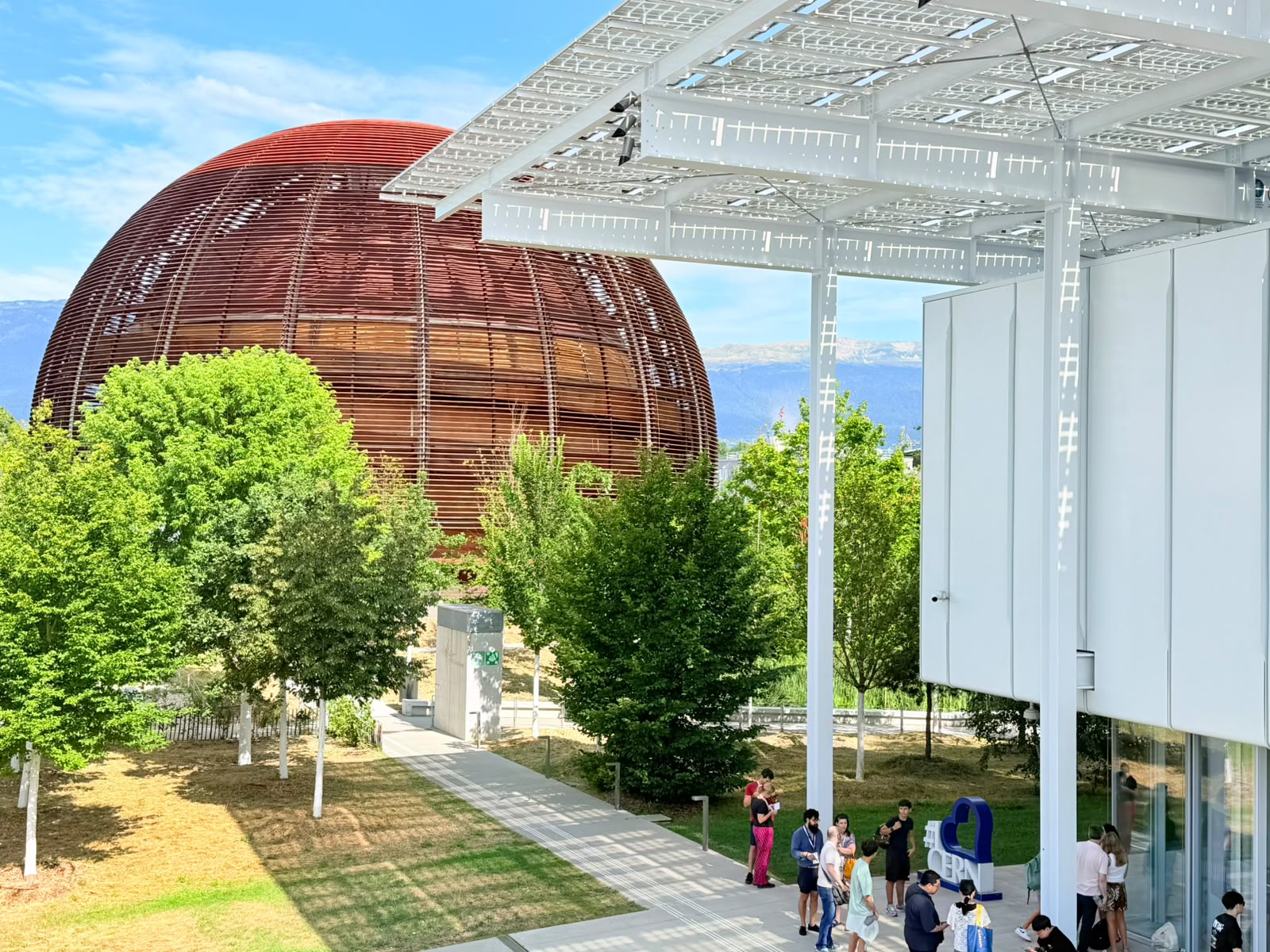A brown-slatted globe building beside a white solar-roofed structure at a campus