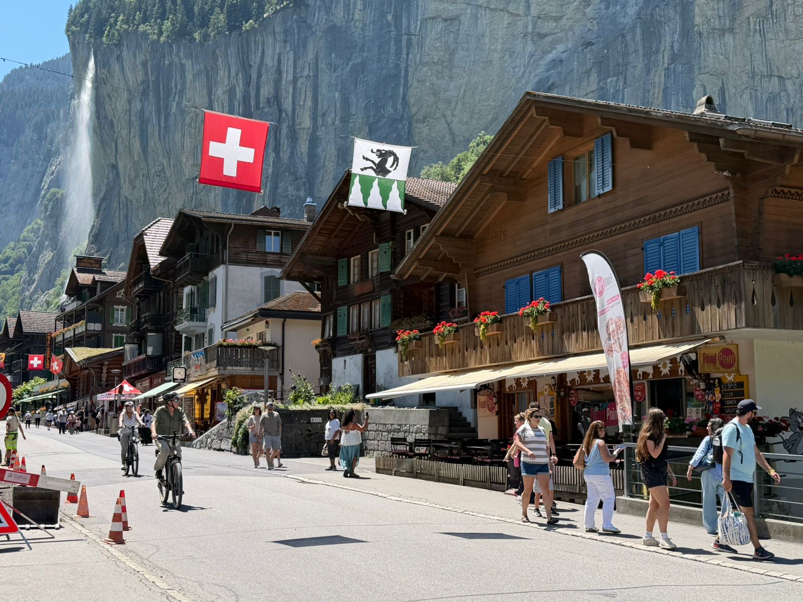 An alpine village street beneath steep cliffs and a waterfall