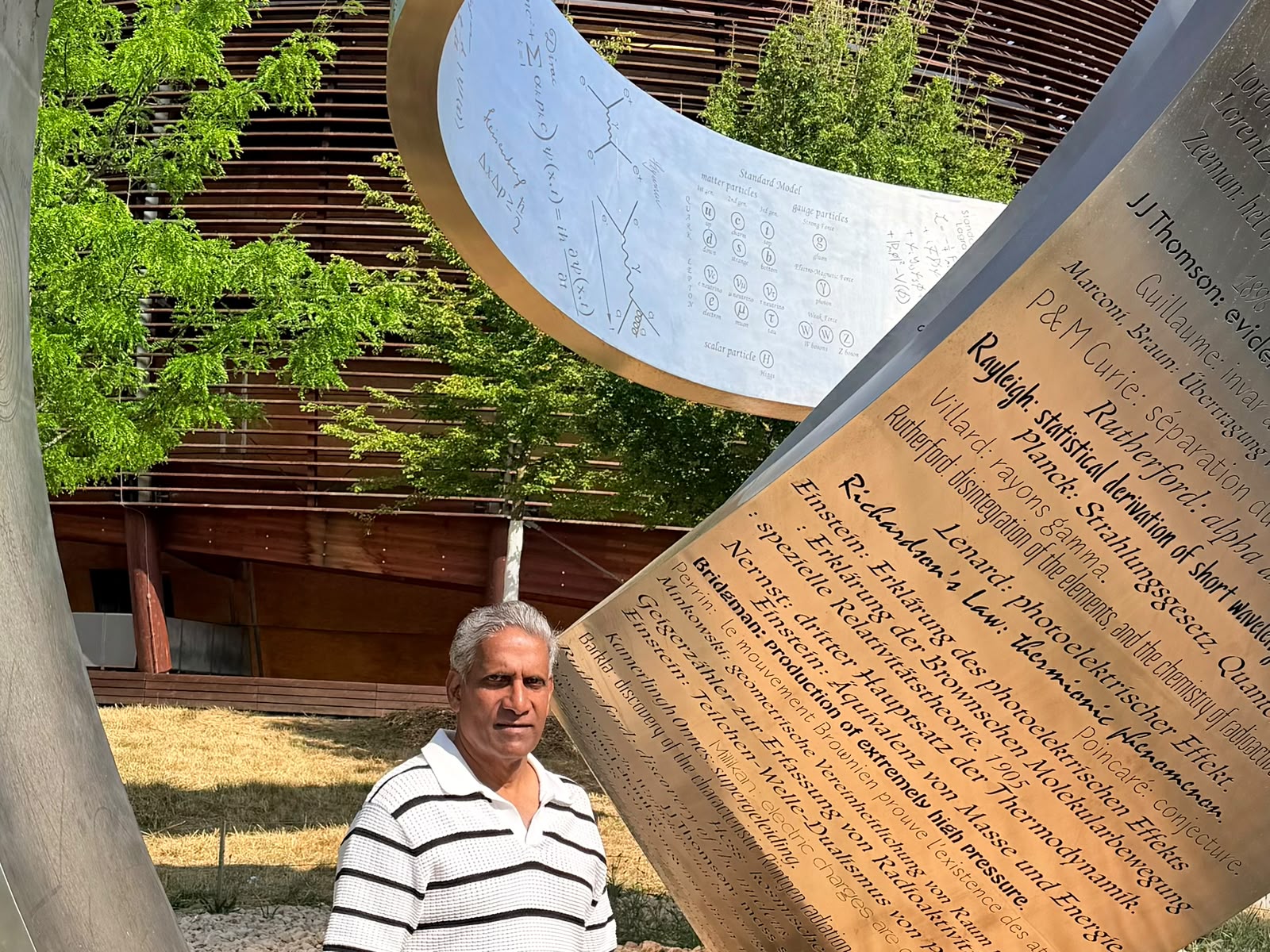 A figure before a curved metallic monument engraved with scientific formulas and names